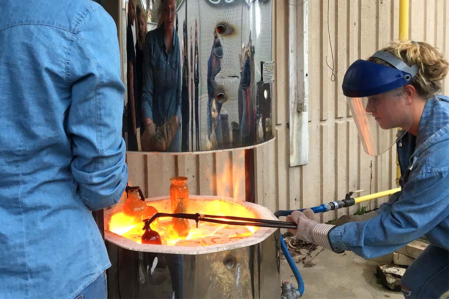 Art student using tongs to remove glowing hot pottery from a raku kiln.