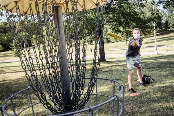 Young man throwing a disc into 1st hole basket of the UW-Green Bay Disc Golf Course