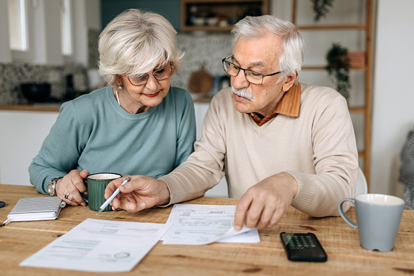 A pair of older adults seated at a table reviewing financial paperwork.