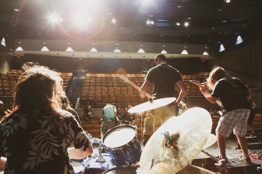 Students play drums, guitar and bass guitar on stage