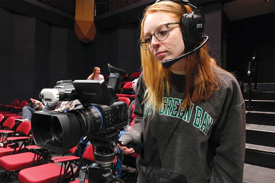 A student wearing head phones while using a high quality video camera.