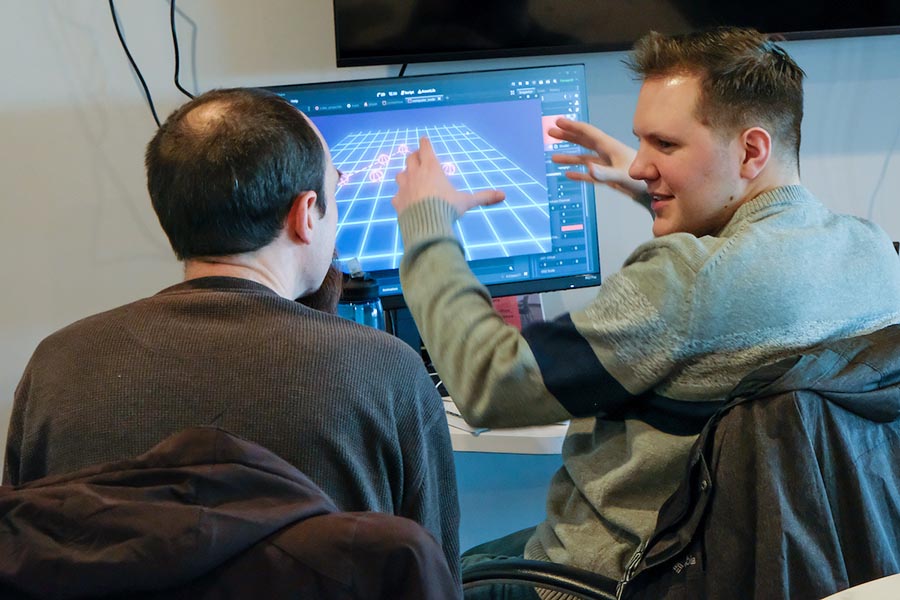 Two males conversing in front of a computer screen