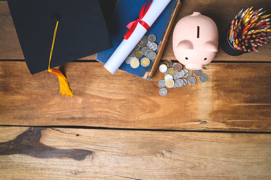 Loose change, graduation cap, diploma, piggy pank and pencils on desk