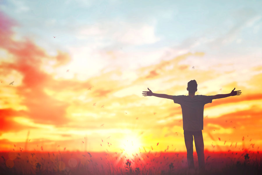 Man looks into the sunrise with outstretched arms