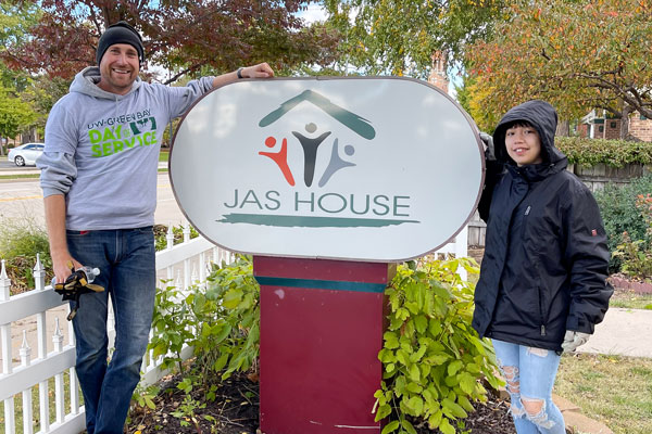 Two people posing next to Jas House sign